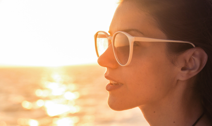 Junge Frau mit Sonnenbrille bei Sonnenuntergang am Meer