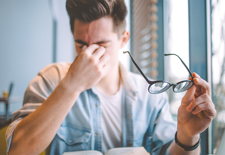 Junger Mann hat Schmerzen beim Lesen mit Brille