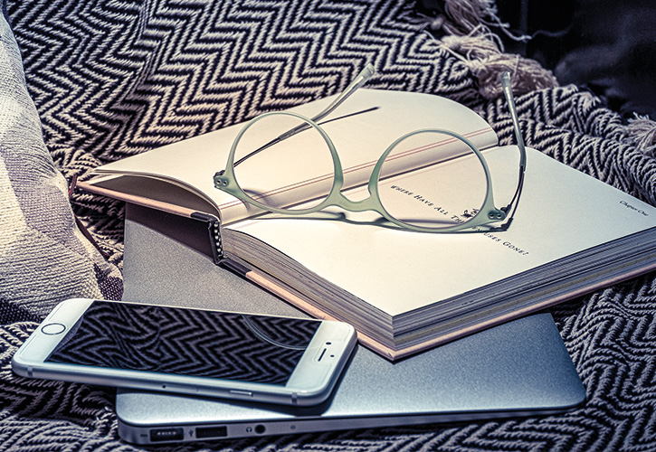 Brille auf aufgeschlagenem Buch, Smartphone und Laptop